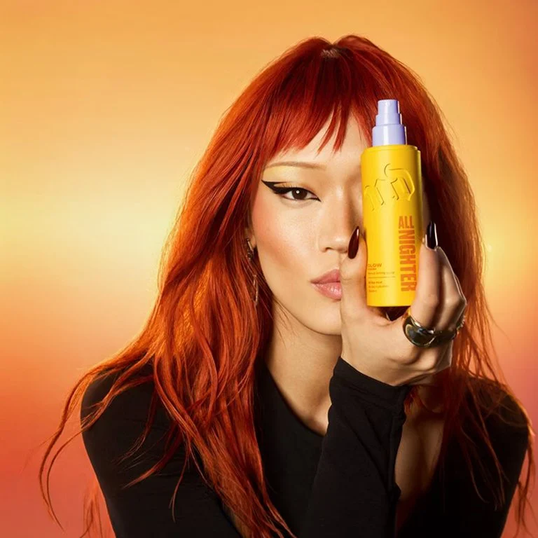 Makeup Woman with red hair holding a bottle of Urban Decay All Nighter Glow Waterproof Setting Spray