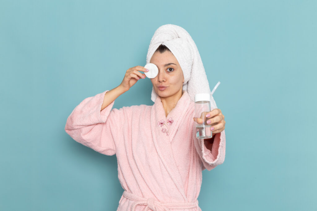 Blog front view young female pink bathrobe cleaning her face from make up blue wall shower cleaning beauty selfcare cream