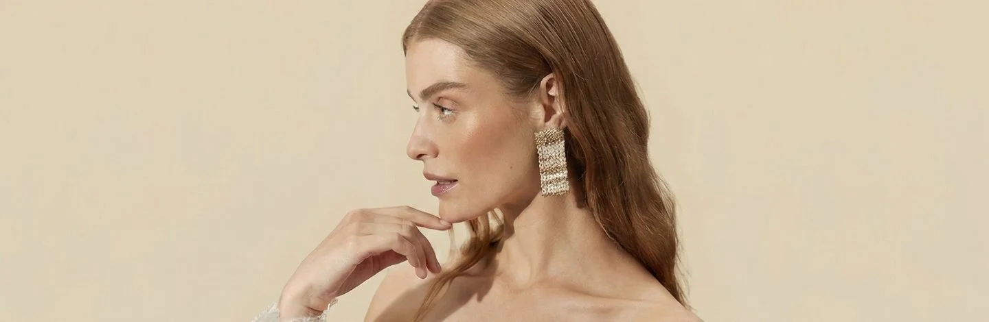Makeup Woman’s side profile, wearing large gold earrings, an off the shoulder top, who has glowing skin